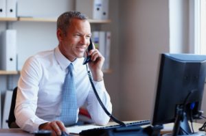 Happy mature business man using computer while talking on phone in the office